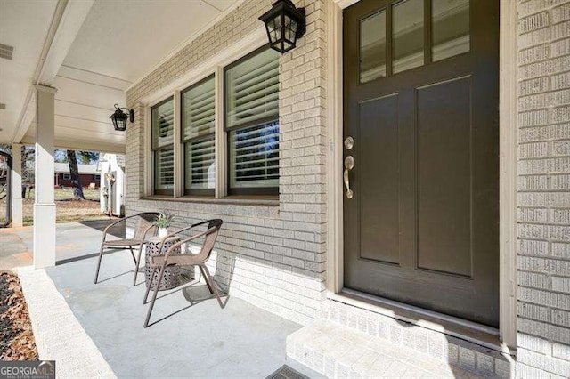 doorway to property featuring brick siding and a porch