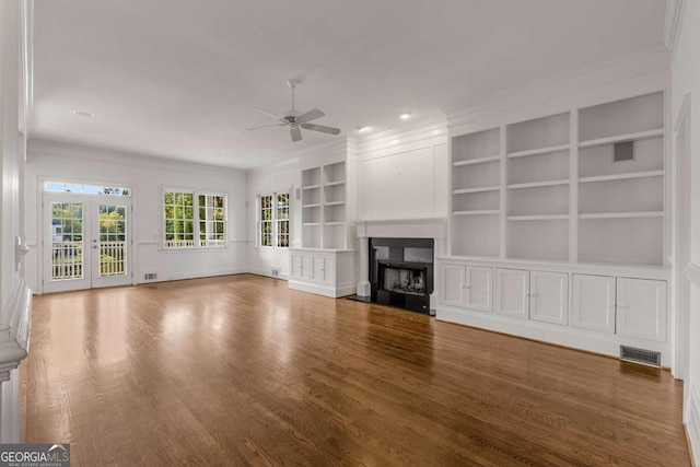 unfurnished living room with a fireplace, visible vents, wood finished floors, and ornamental molding