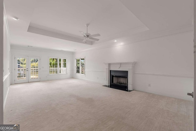 unfurnished living room featuring a fireplace with flush hearth, carpet flooring, a ceiling fan, a raised ceiling, and crown molding