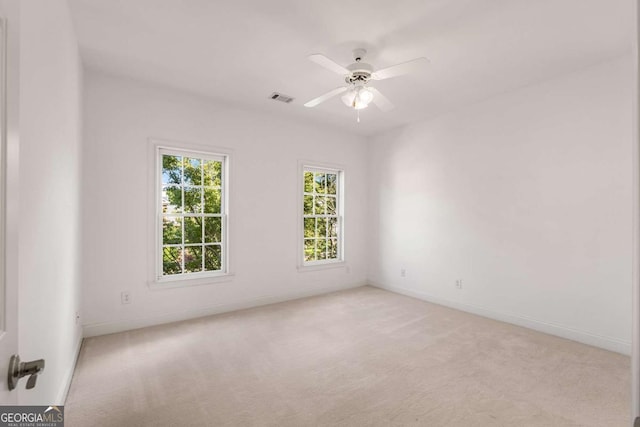 empty room featuring light colored carpet, visible vents, ceiling fan, and baseboards