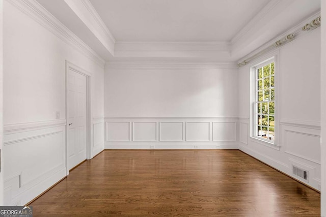 spare room featuring visible vents, a raised ceiling, wainscoting, wood finished floors, and crown molding
