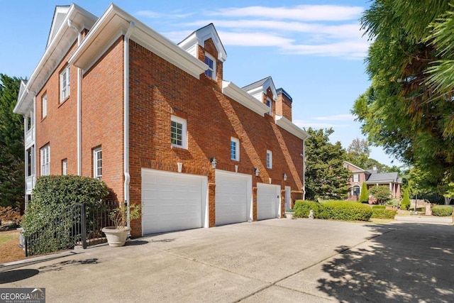 view of property exterior featuring concrete driveway, brick siding, a chimney, and an attached garage
