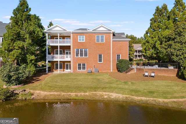 rear view of property featuring a lawn, a water view, fence, and a balcony