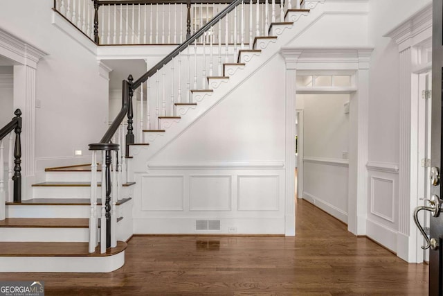 stairway featuring a high ceiling, wood finished floors, visible vents, and a decorative wall