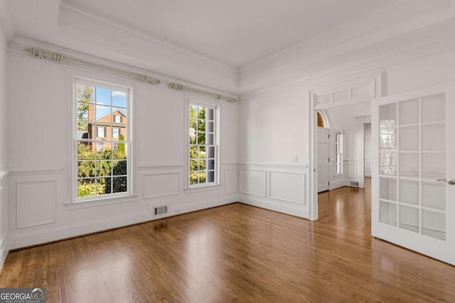 empty room featuring ornamental molding, wood finished floors, visible vents, and a decorative wall