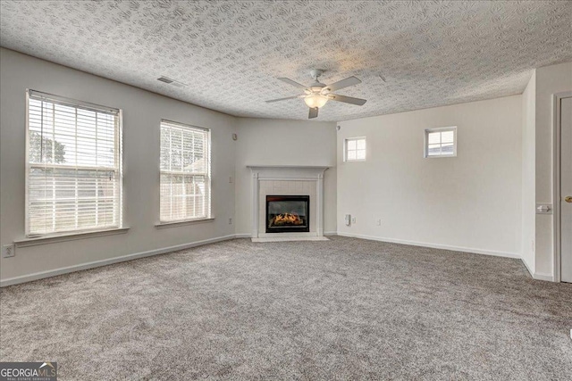 unfurnished living room featuring a fireplace, visible vents, carpet flooring, a textured ceiling, and baseboards