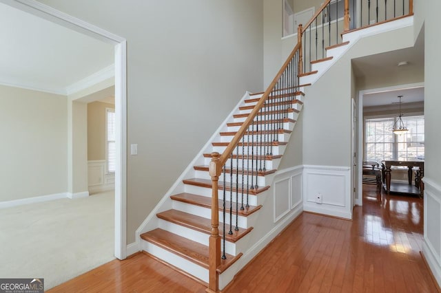 stairs with hardwood / wood-style flooring, a decorative wall, a towering ceiling, ornamental molding, and wainscoting