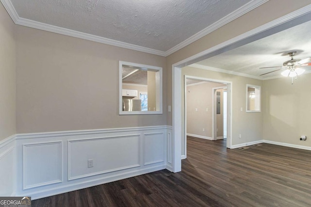 empty room featuring wainscoting, ceiling fan, ornamental molding, dark wood-type flooring, and a textured ceiling