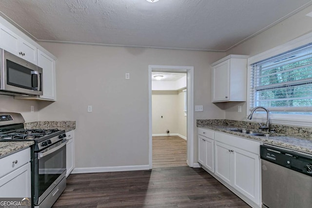 kitchen with dark wood-style flooring, stainless steel appliances, white cabinetry, a sink, and light stone countertops