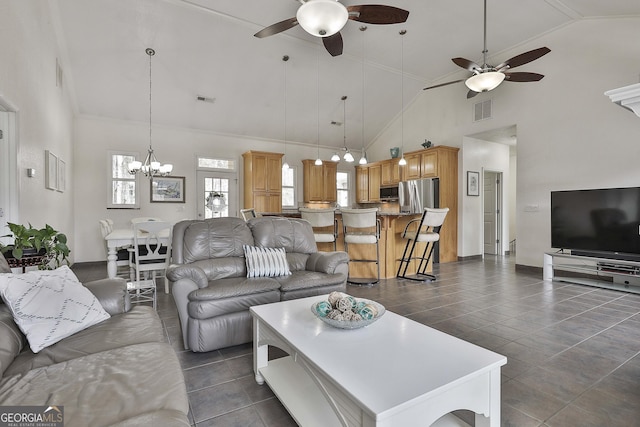 living area featuring high vaulted ceiling, ceiling fan with notable chandelier, visible vents, and dark tile patterned flooring