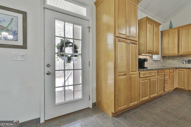 kitchen with vaulted ceiling, dark tile patterned floors, dark stone countertops, and decorative backsplash