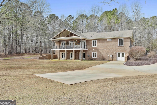 view of front facade with driveway, brick siding, a balcony, and a front yard