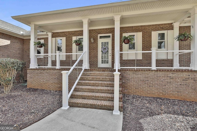 doorway to property featuring covered porch and brick siding