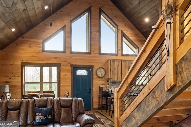 living room featuring high vaulted ceiling, wooden ceiling, wood walls, and stairway