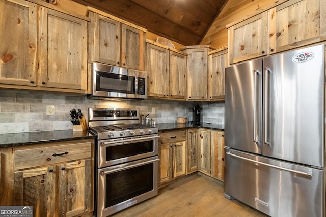 kitchen featuring lofted ceiling, light wood-style flooring, appliances with stainless steel finishes, tasteful backsplash, and dark stone countertops