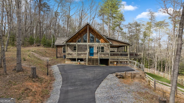 view of front facade with driveway, stone siding, fence, and a wooden deck