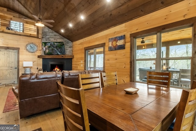 dining room with ceiling fan, a stone fireplace, wooden walls, wood finished floors, and wood ceiling