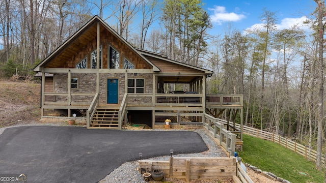 chalet / cabin with stone siding, stairway, fence, and driveway