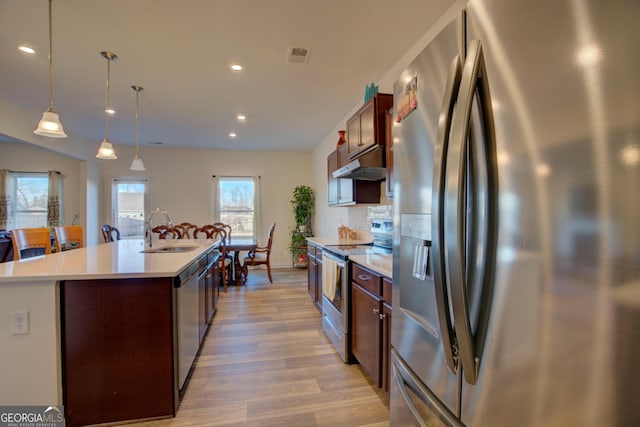 kitchen with stainless steel appliances, light countertops, a sink, an island with sink, and under cabinet range hood