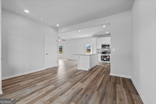 kitchen with open floor plan, wood finished floors, stainless steel appliances, white cabinetry, and recessed lighting