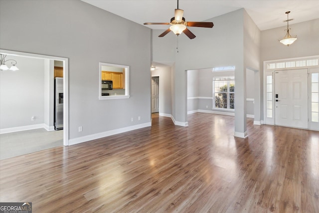 unfurnished living room featuring ceiling fan, a towering ceiling, baseboards, and wood finished floors