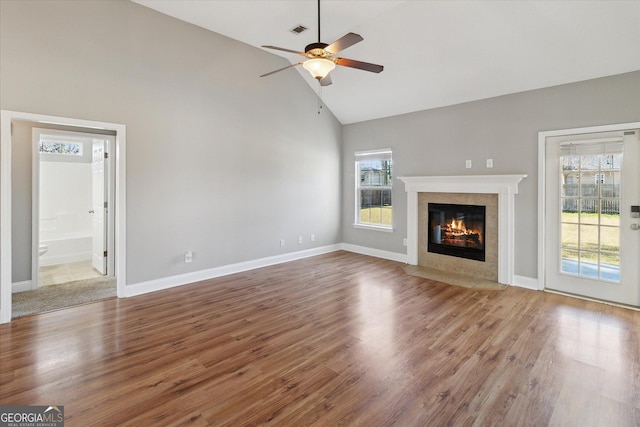 unfurnished living room featuring visible vents, a ceiling fan, a tiled fireplace, wood finished floors, and high vaulted ceiling