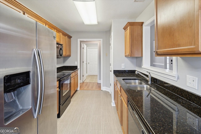 kitchen featuring black electric range, brown cabinetry, a sink, dark stone counters, and stainless steel fridge
