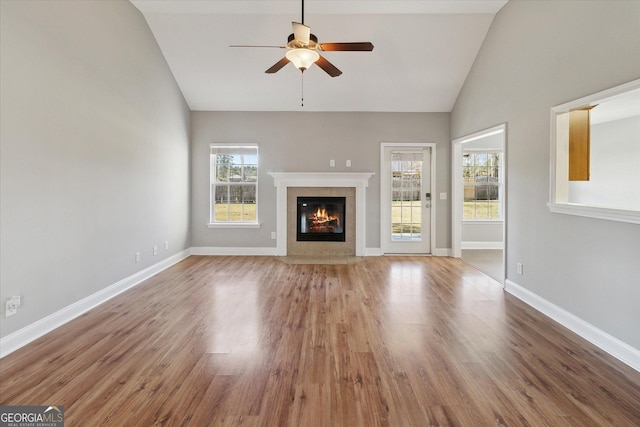 unfurnished living room with high vaulted ceiling, wood finished floors, a ceiling fan, a high end fireplace, and baseboards
