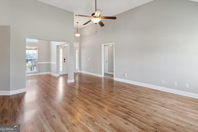 unfurnished living room with a towering ceiling, wood finished floors, a ceiling fan, and baseboards