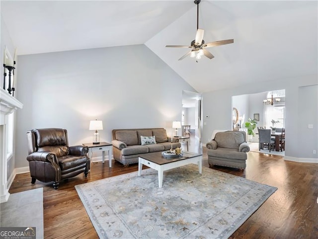 living area with baseboards, a fireplace with flush hearth, wood finished floors, high vaulted ceiling, and ceiling fan with notable chandelier