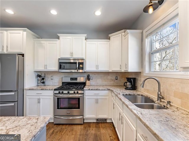 kitchen with decorative backsplash, appliances with stainless steel finishes, white cabinets, a sink, and wood finished floors