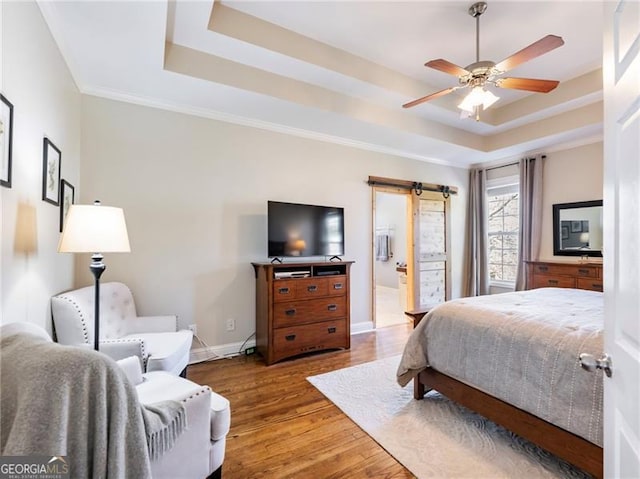 bedroom with baseboards, a barn door, a tray ceiling, and wood finished floors