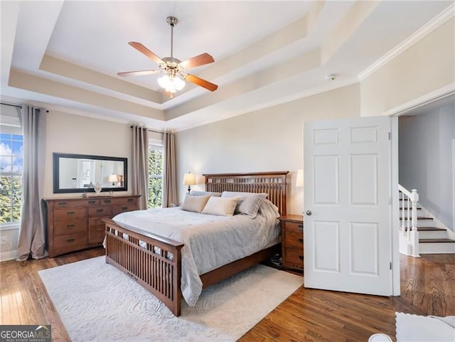 bedroom with a ceiling fan, a raised ceiling, ornamental molding, and hardwood / wood-style flooring