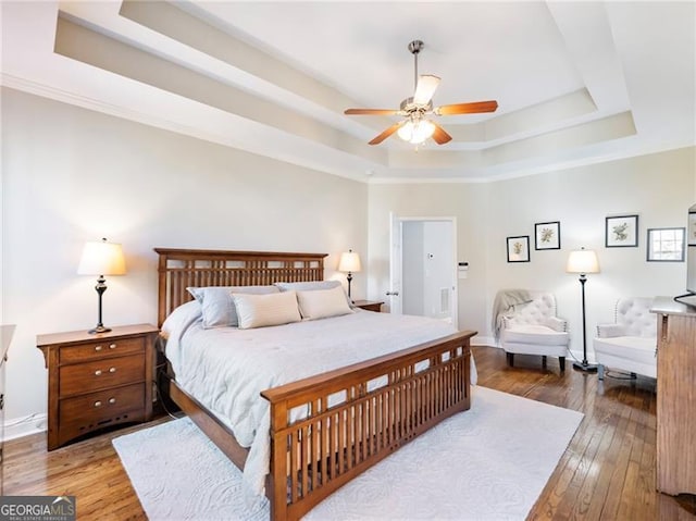 bedroom featuring a tray ceiling, wood-type flooring, ceiling fan, and baseboards