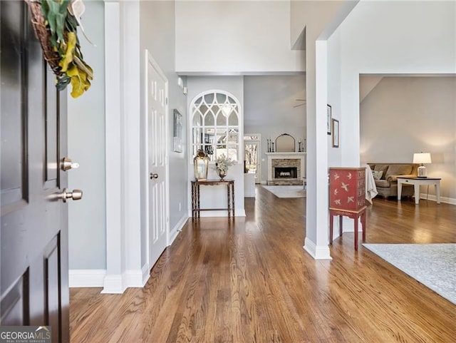 foyer entrance with a towering ceiling, baseboards, wood finished floors, and a stone fireplace