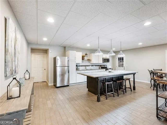 kitchen with white cabinets, an island with sink, appliances with stainless steel finishes, a breakfast bar, and light wood-type flooring