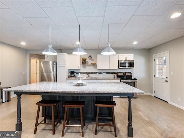 kitchen featuring a breakfast bar area, stainless steel appliances, a spacious island, white cabinets, and a sink