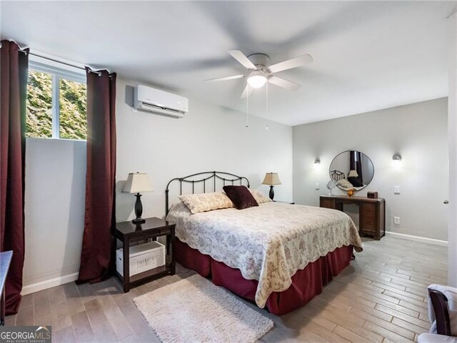 bedroom featuring a wall unit AC, light wood finished floors, and baseboards