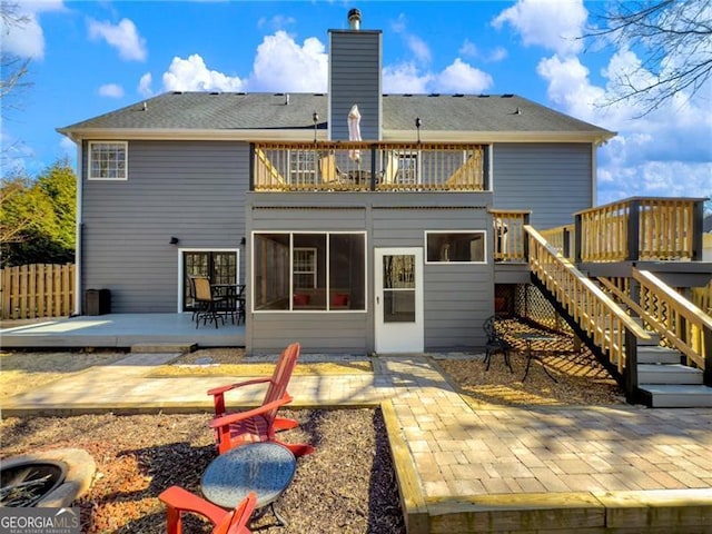 rear view of house featuring a balcony, a chimney, stairway, fence, and a wooden deck