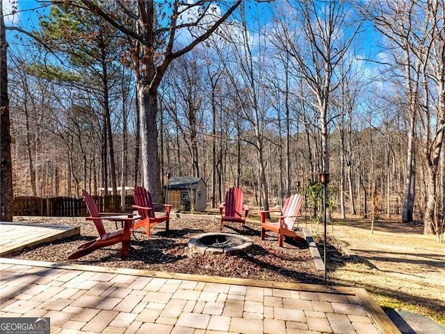 view of patio featuring fence, a fire pit, a wooded view, and an outbuilding