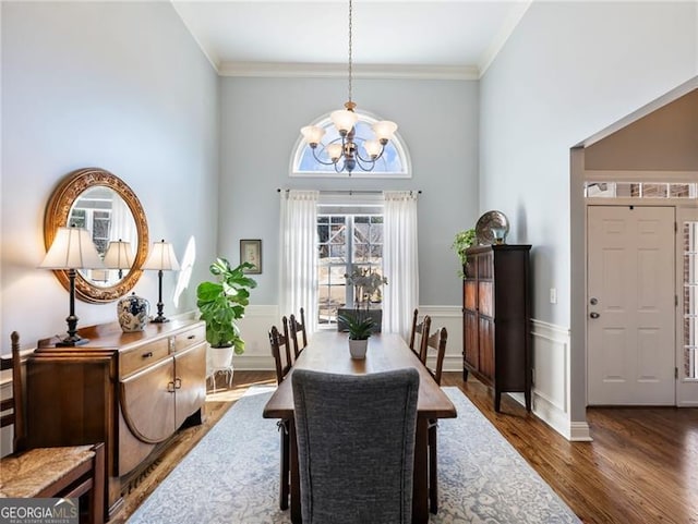 dining space with a wainscoted wall, crown molding, wood finished floors, and an inviting chandelier