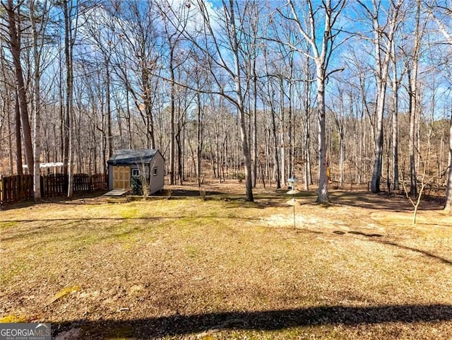 view of yard with an outbuilding, fence, a wooded view, and a storage shed