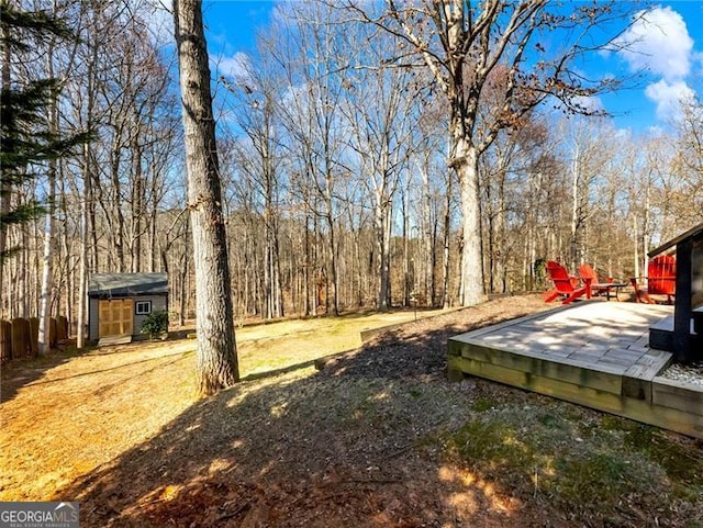 view of yard featuring an outbuilding, a forest view, a deck, and fence