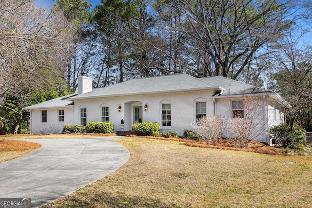 ranch-style home featuring brick siding, driveway, a chimney, and a front lawn