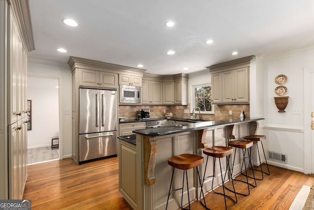 kitchen featuring a breakfast bar area, stainless steel appliances, visible vents, a sink, and a peninsula