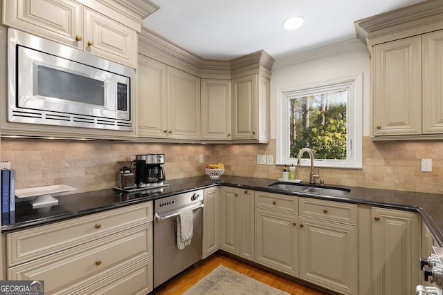 kitchen with light wood finished floors, decorative backsplash, cream cabinets, appliances with stainless steel finishes, and a sink