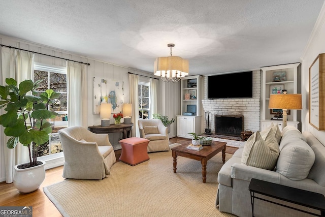 living room featuring a brick fireplace, a chandelier, a textured ceiling, and wood finished floors