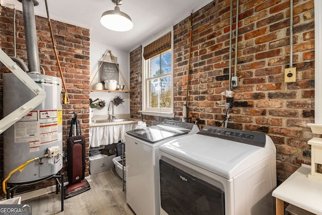 washroom with laundry area, washer and clothes dryer, brick wall, light wood-type flooring, and water heater