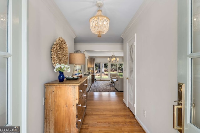 corridor featuring an inviting chandelier, baseboards, light wood-style floors, and crown molding