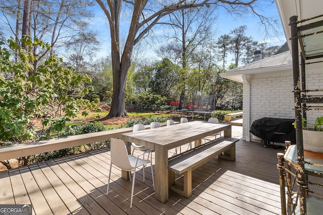 deck featuring outdoor dining space, a trampoline, and area for grilling